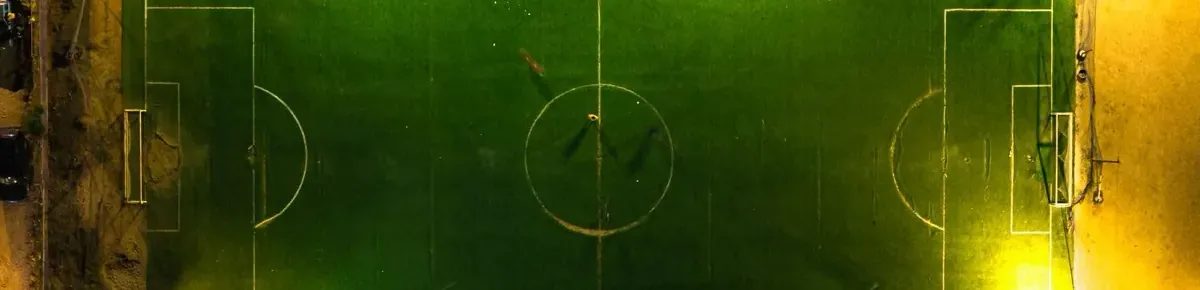 A floodlit five-a-side pitch photographed from directly above at night, its line markings picked out by the lights.